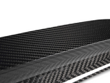 A close-up view of a glossy carbon fiber texture, displaying its distinctive woven pattern. The material appears sleek and polished, set against a plain, light background.