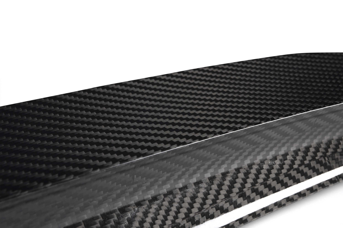 A close-up view of a glossy carbon fiber texture, displaying its distinctive woven pattern. The material appears sleek and polished, set against a plain, light background.
