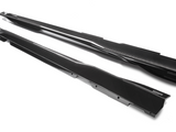 Two sleek, black carbon fiber side skirts lie parallel on a white surface. 
