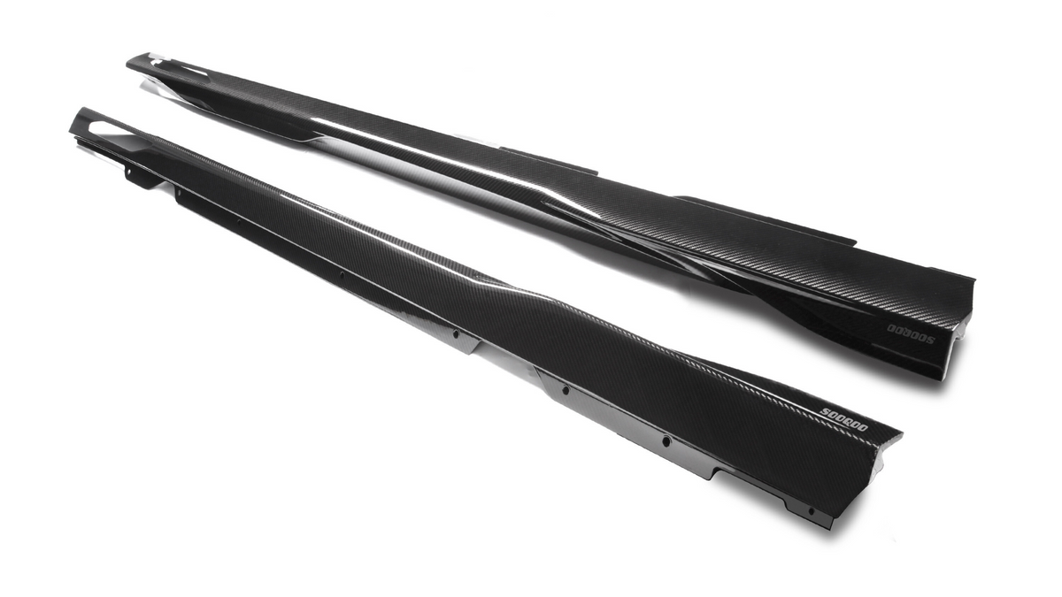 Two sleek, black carbon fiber side skirts lie parallel on a white surface. "500600" is printed on one of the skirts, adding a branded detail to enhance a car’s aerodynamic profile.