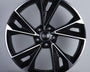 A glossy black alloy wheel, featuring a stylish multi-spoke design, stands upright against a light gray background. The center displays the Audi logo with four interlocking rings.