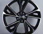 A glossy black car wheel with five split spokes features a central circle displaying four interlinked rings. It rests against a plain gray background, highlighting its modern design.