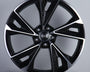 A black and silver alloy wheel, featuring a prominent logo with four interlinked circles at the center, is displayed against a plain gray background.