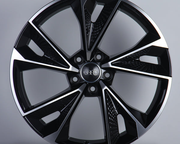 A sleek, glossy black alloy wheel with a multi-spoke design featuring the Audi logo at its center, displayed against a plain gray background on a white platform.
