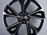 A glossy black alloy wheel with silver accents featuring five wide spokes and a central emblem displaying four interlocking rings. It is displayed on a plain gray background.
