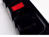A black car bumper features a small rectangular red reflector and a circular hole, set on a white background.