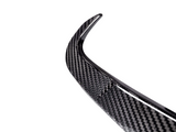 A curved carbon fiber piece, possibly a car spoiler, is shown against a plain, white background, highlighting its textured pattern and sleek design.