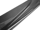 A shiny carbon fiber strip with a textured, checkered pattern is angled diagonally, reflecting light against a plain white background.
