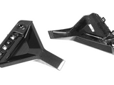 Carbon fiber components lying on a white surface; one has a rectangular grid pattern, and the other features mounting clips and a small label.