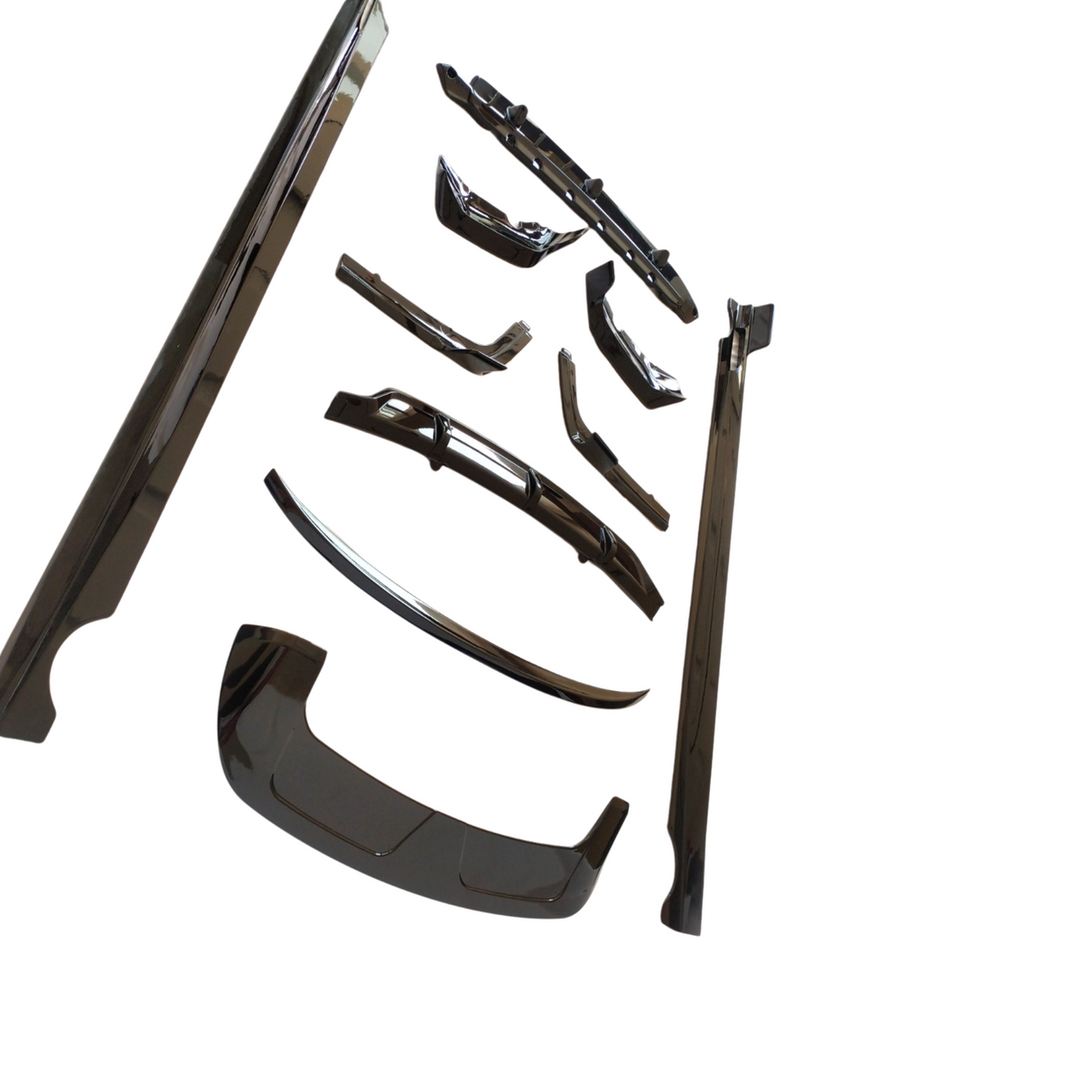 Assorted shiny black car body parts, including bumpers and trim pieces, are neatly arranged on a white background, emphasizing their polished surfaces and intricate designs.