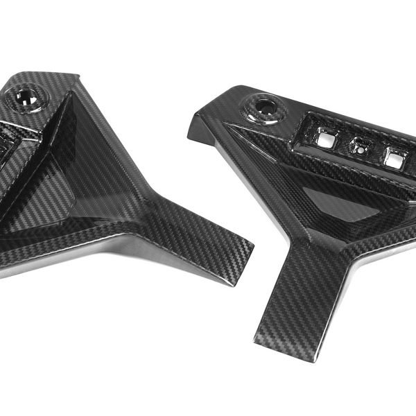 Two carbon fiber car parts, featuring angular designs with multiple slots and a bolt hole, are positioned against a plain white background.
