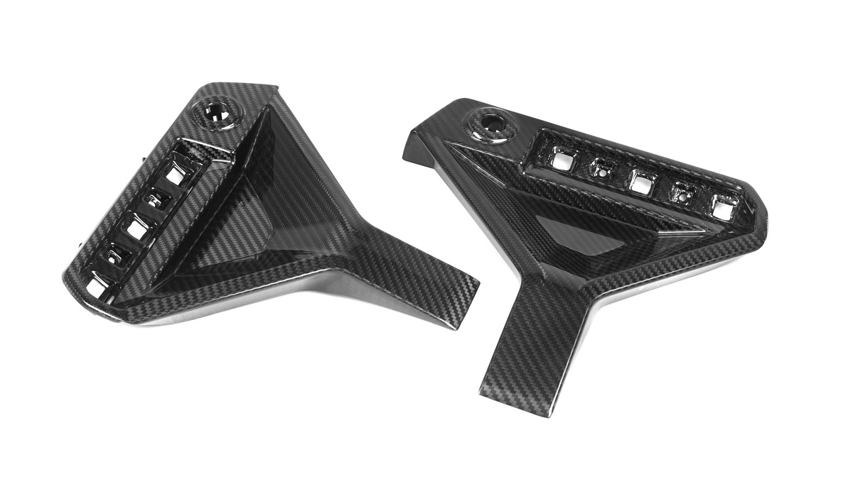 Two carbon fiber car parts, featuring angular designs with multiple slots and a bolt hole, are positioned against a plain white background.