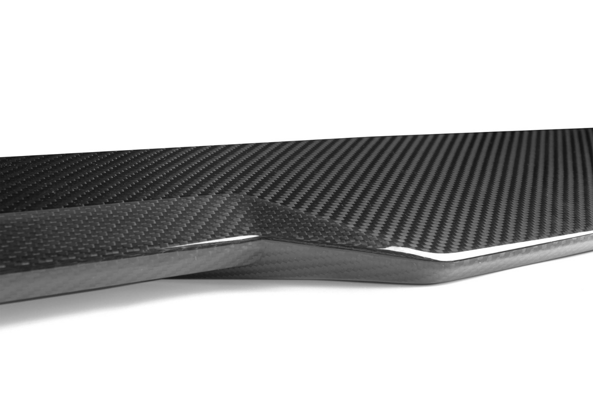 Carbon fiber panel with a textured, glossy surface, lies flat and neatly angled. The background is a plain, white setting, emphasizing the panel’s sleek and modern design.