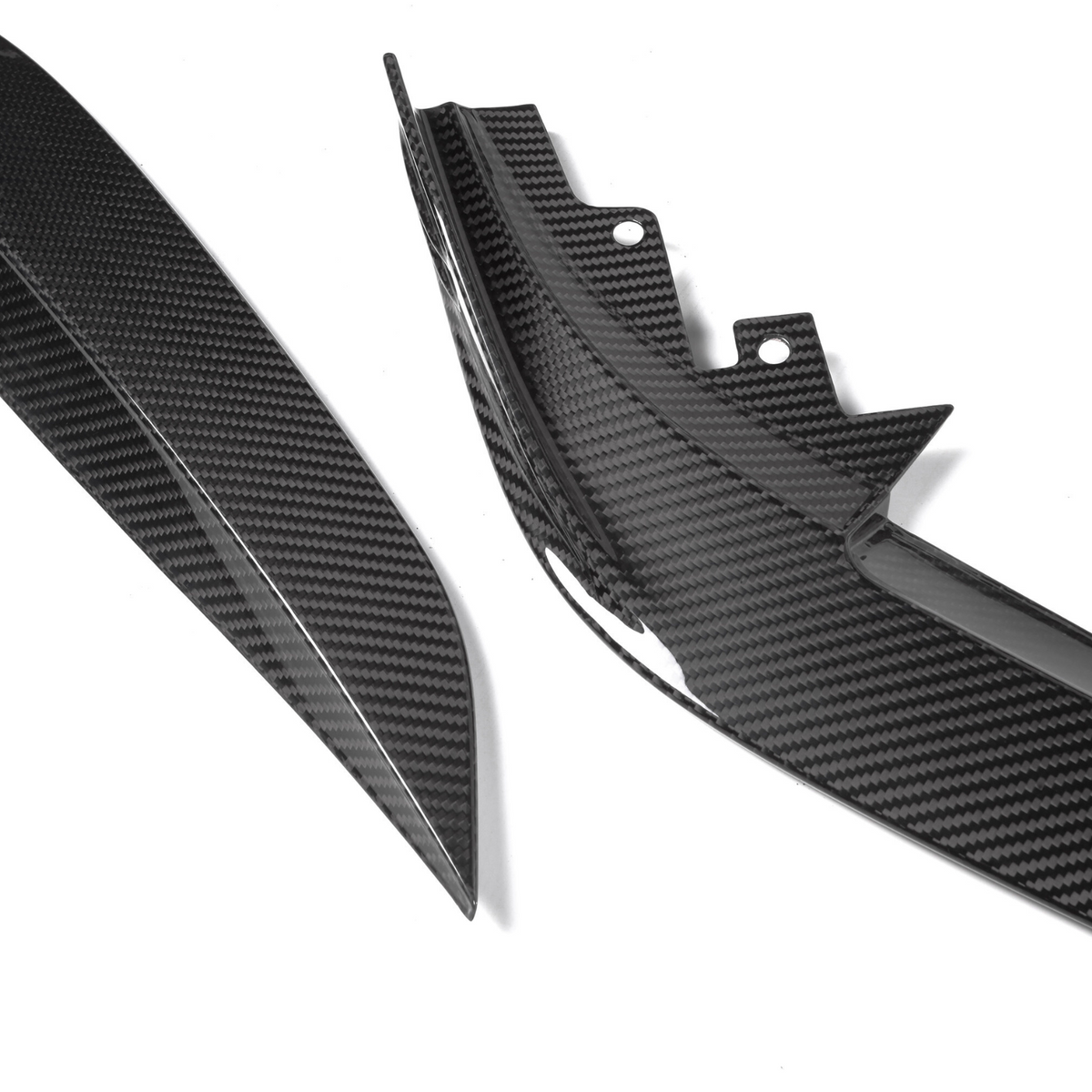 Two carbon fiber car body parts lie on a white surface, showcasing sleek, angular designs and the distinctive checkered pattern typical of carbon fiber material.