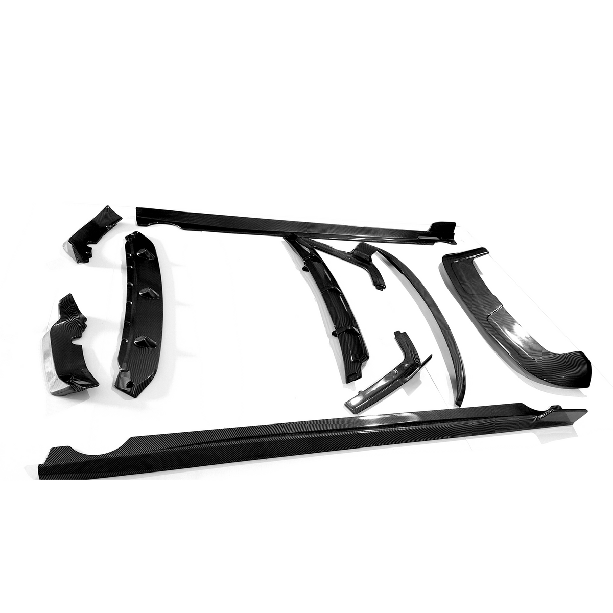 Various carbon fiber car parts lie scattered on a white surface, including spoilers and side skirts, arranged in an orderly fashion, highlighting their sleek, aerodynamic design.