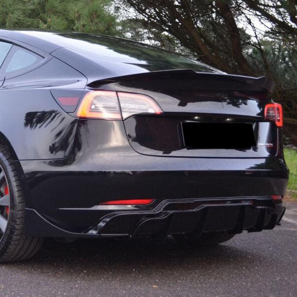 A sleek, black car with tinted windows is parked on a road, surrounded by green trees. The rear design includes distinct taillights and a spoiler, conveying a modern, sporty appearance.