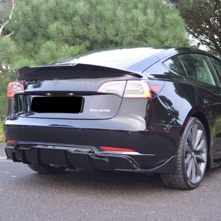 A black car is parked on a road, featuring visible "Dual Motor" text on the trunk, with lush green trees in the background.