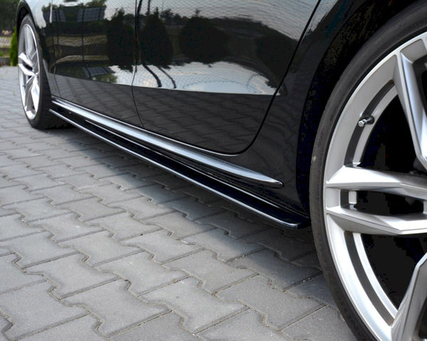 A black car, parked on interlocking brick pavement, displays sleek silver rims and reflective doors, surrounded by greenery in the background.