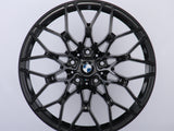 A black alloy wheel with a complex, multi-spoke design is displayed against a plain white background. The center features the BMW logo, surrounded by intricate patterns.
