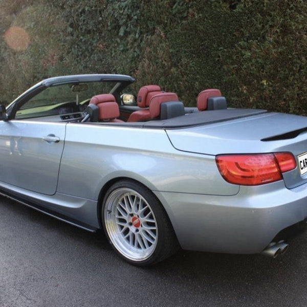 Convertible car parked, top down revealing red interior, surrounded by hedge and grass. License plate reads "CARBON ACCENTS."