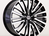 A car wheel features a black and silver multi-spoke design with a central Volkswagen emblem, displayed against a plain white background.