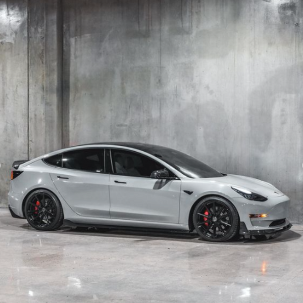 A sleek, silver electric car with black wheels parked on a polished concrete floor, set against a gray, industrial-style wall.
