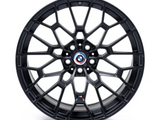 A black alloy wheel with a complex geometric spoke design features a BMW emblem at the center. It rests on a plain white background.
