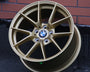 A gold BMW car wheel lies against a brick wall. The wheel is detailed and has a logo at its center. The design is sleek and modern.