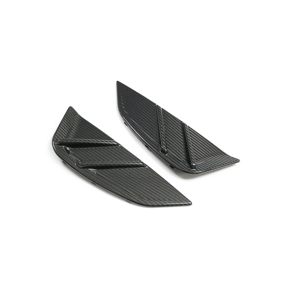 Two black carbon-fiber automotive splitters, each with angular shapes and grooves, are placed on a plain white surface, suggesting high-performance vehicle components.
