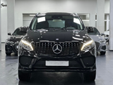 A black Mercedes-Benz SUV stands prominently with headlights on, inside a showroom, flanked by two other black cars in the background.
