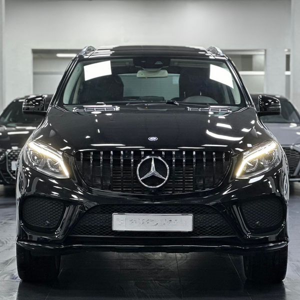 A black Mercedes-Benz SUV stands prominently with headlights on, inside a showroom, flanked by two other black cars in the background.