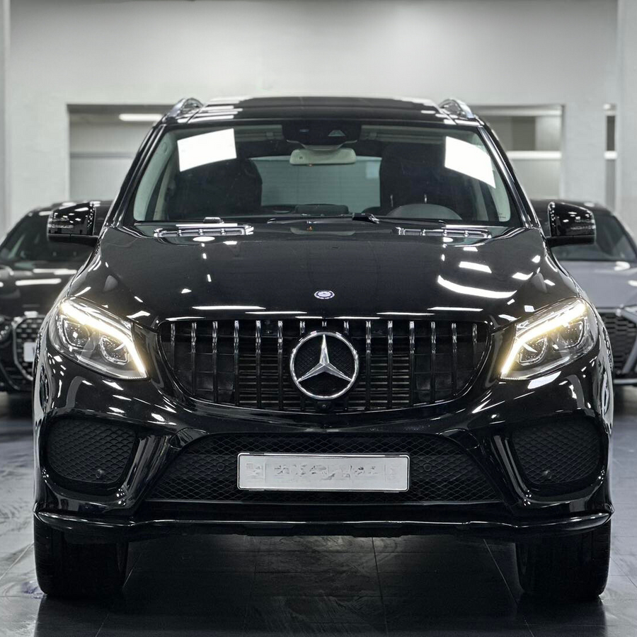 A black Mercedes-Benz SUV stands prominently with headlights on, inside a showroom, flanked by two other black cars in the background.