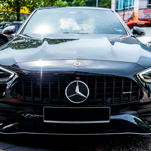 A black Mercedes-Benz AMG car is parked outdoors on a sunny day, surrounded by other vehicles. The brand logo is prominently displayed on the grille.