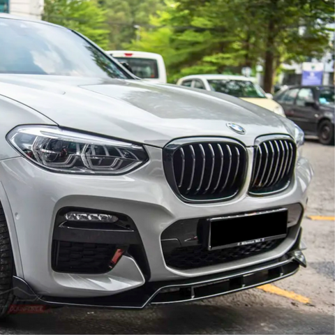 A white BMW car is parked on a street, surrounded by other vehicles and lined with green trees in the background.