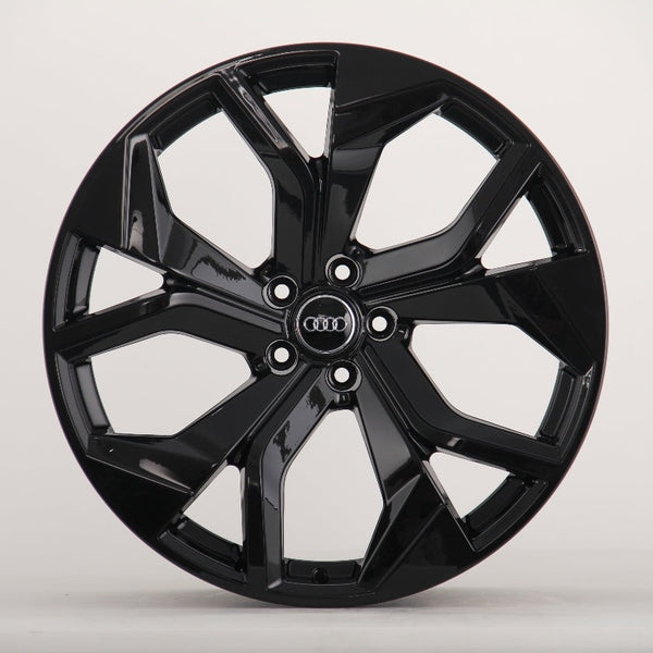 A glossy black alloy wheel with a five-spoke design featuring the Audi logo at the center, sits against a plain white background.