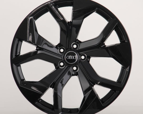A shiny black, multi-spoke alloy wheel with an "Audi" emblem in the center is displayed against a plain, light gray background.