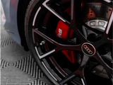 A black car wheel with an Audi logo features a red brake caliper marked 