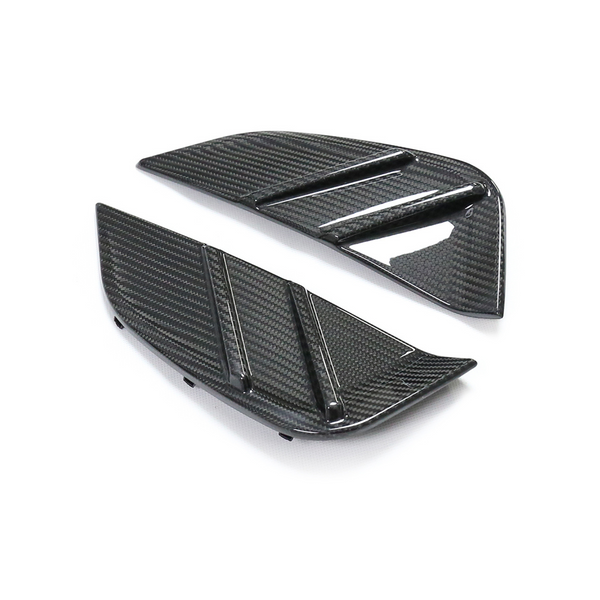 Two black carbon fiber car vents, angled and textured, with horizontal ridges. They rest on a plain white background, emphasizing their sleek, modern design.