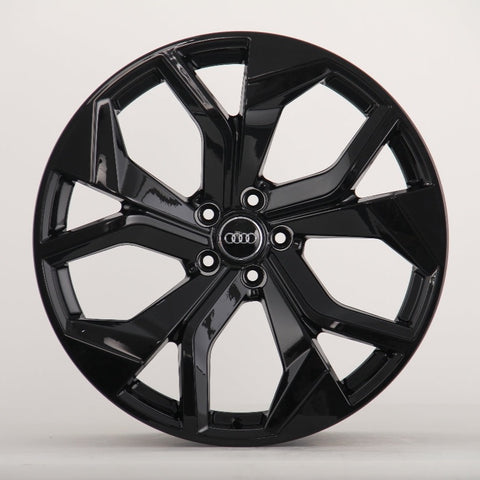 A glossy black alloy wheel with a multi-spoke design. The Audi logo is centered on the hub. It's set against a plain, light grey background.