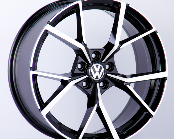 A black and silver alloy wheel with a Volkswagen logo in the center is displayed against a plain white background, highlighting the wheel's modern, geometric spoke design.