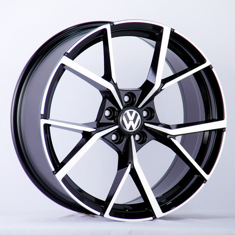 A black and silver alloy wheel with a Volkswagen logo in the center is displayed against a plain white background, highlighting the wheel's modern, geometric spoke design.