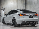 A sleek, white car with illuminated tail lights is stationary in a concrete-walled garage. The 
