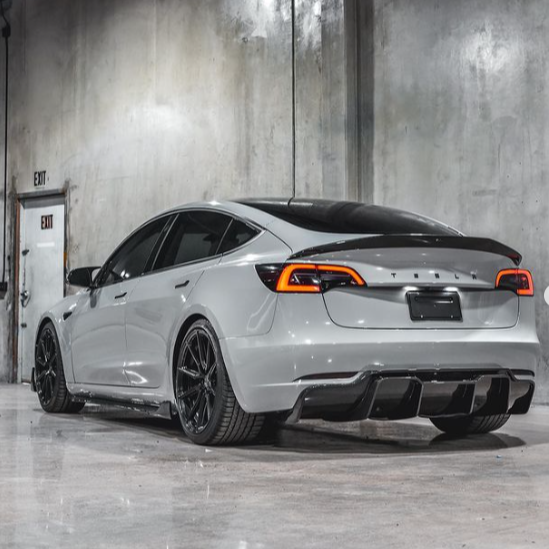 A sleek, white car with illuminated tail lights is stationary in a concrete-walled garage. The "EXIT" sign is visible on a door to the left.