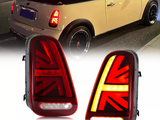 Car taillights display at night, mounted on a Mini Cooper, feature Union Jack design; close-up highlights illuminated red and amber patterns. The vehicle is parked on a city street.