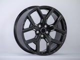 A sleek, glossy black alloy car wheel sits angled, displaying its intricate spoke design against a neutral gray background.