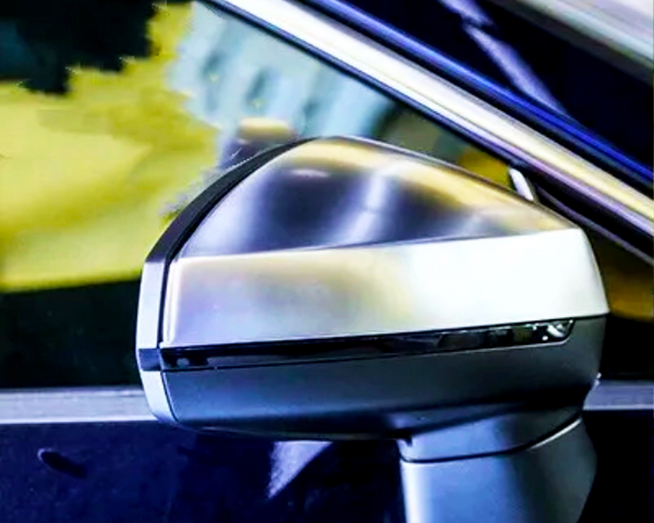 A car's side-view mirror reflects light in a close-up shot, set against the vehicle's shiny blue body and a blurred, yellow-tinted background.