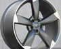 A sleek, metallic alloy wheel with a five-spoke design rests on a flat surface against a plain, light-colored wall background, showcasing its modern, polished appearance.