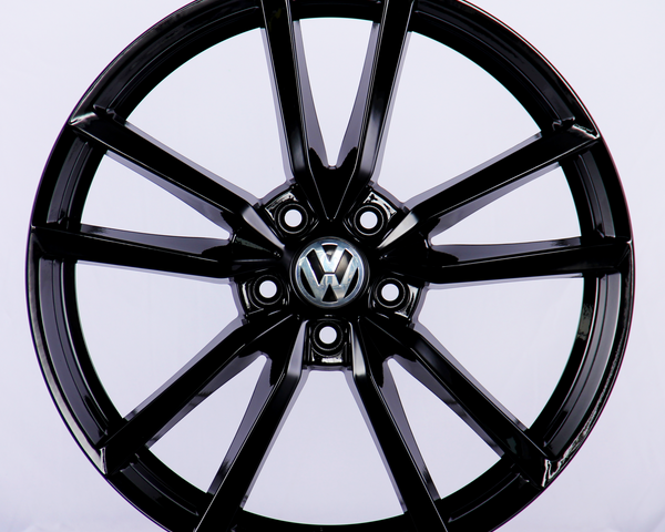 A black alloy car wheel is displayed with a five-spoke design, featuring the Volkswagen logo in the center, set against a plain white background.
