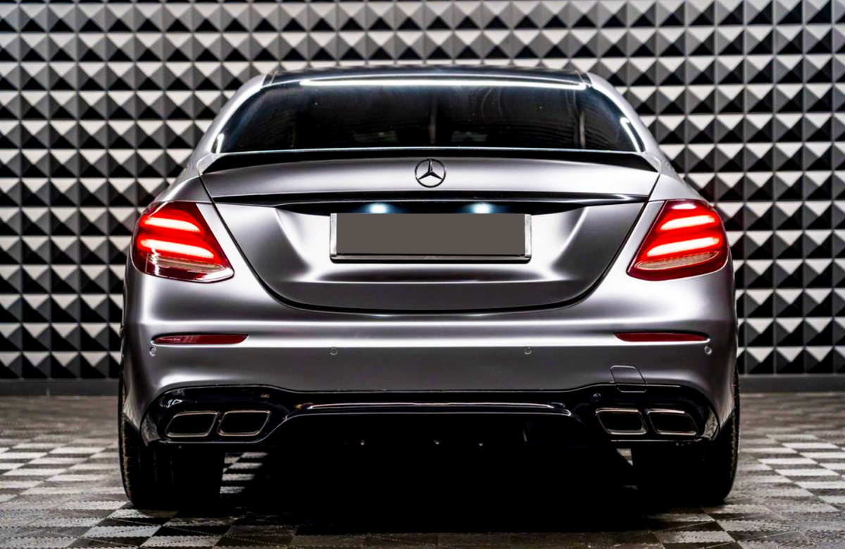 A sleek car with illuminated taillights is parked, facing a geometric-patterned wall in a showroom-like setting.