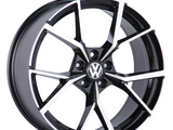 A black and silver alloy wheel with a geometric pattern, displaying the Volkswagen logo in the center, is positioned against a plain white background.